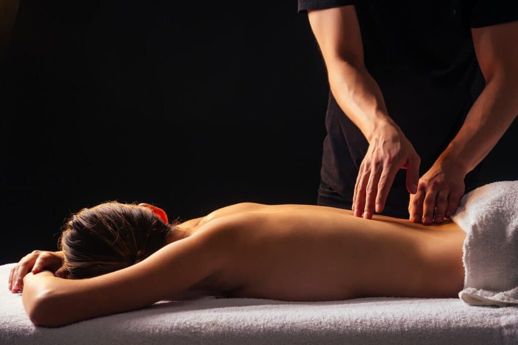 Masseur hands doing back massage to client in spa center in dark room